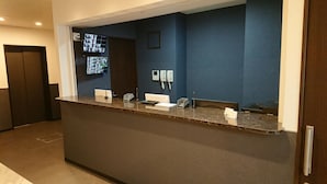 A reception desk with a flat-screen TV, a telephone, and a digital display. - Hotel Chuo Bridge (Osaka)