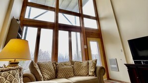 A living room with a large window, a sofa, a lamp, a TV, and a coffee table. - 3B Condo Overlooking Sugar Ski Slopes! (Sugar Mountain)