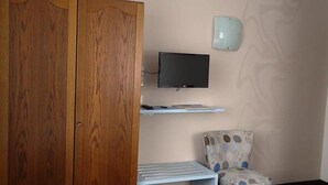 Una stanza con un'armadio in legno, una televisione a parete, una sedia a motivi decorativi e una mensola con dei libri.
