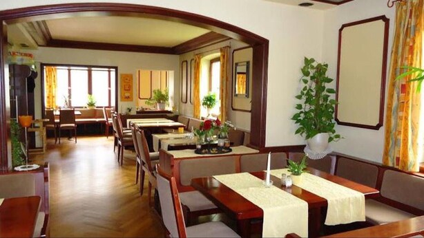 Zona pranzo con tavoli e sedie in legno, piante in vaso e vista sulla stanza adiacente.