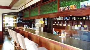 Un’area bar con un lungo bancone, diversi sgabelli da bar e una varietà di bottiglie e bicchieri sugli scaffali.
