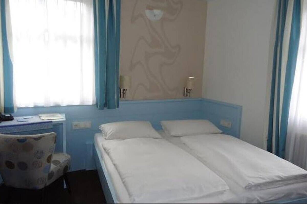 Habitación de hotel con cama, una silla, un escritorio y una ventana con cortinas.