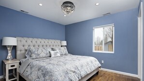 A bedroom with a tufted headboard, a large bed with patterned bedding, two bedside lamps, and a window with a view of a wooden deck. - Beautiful Home in Willits! (Basalt)