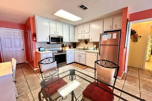 Compact kitchen with a glass-top dining table and stainless steel appliances, including a microwave, oven, and refrigerator.
