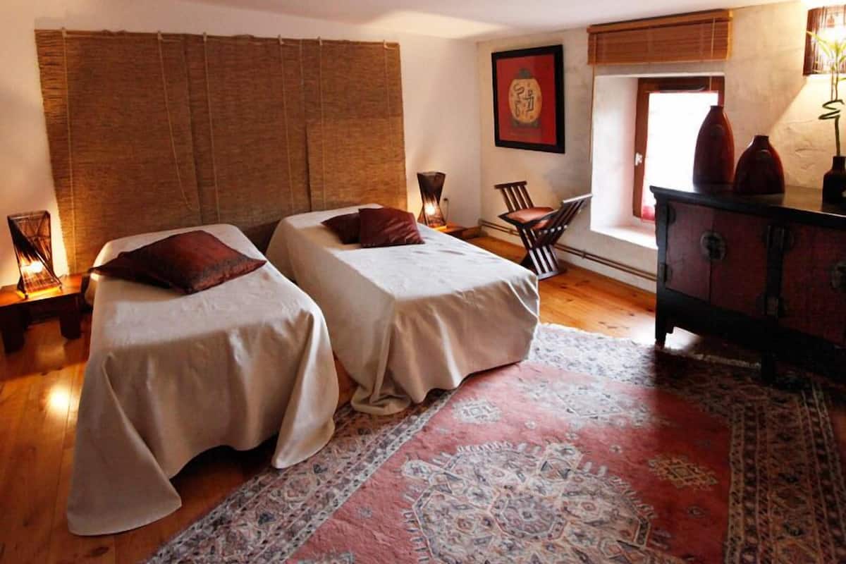 A room with two beds, a wooden floor, a patterned rug, a desk with a chair, and a dresser.