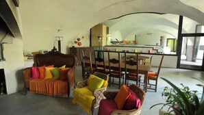 A spacious living area with a dining table and chairs, a sofa with colorful cushions, and a large window providing natural light. - Le Moulinage (Saint-Thomé)