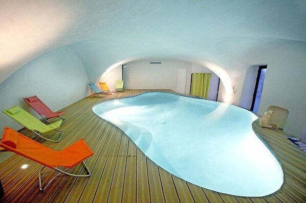 An indoor swimming pool with wooden flooring and colorful lounge chairs.