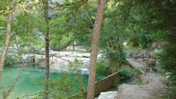 A natural setting with a clear water body, surrounded by trees and a wooden pathway. - Le Moulinage (Saint-Thomé)