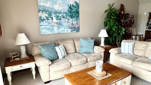 A living room with a beige sofa, two side tables with lamps, a wooden coffee table, and a large landscape painting on the wall. - Relaxing Marvelous Main Channel View! (Lake Ozark)