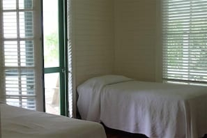 Quarto com duas camas de solteiro, janela com persianas e porta que dá para o exterior.