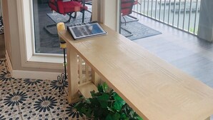 Une pièce avec une table en bois, des chaises rouges et un ordinateur portable. Il y a une fenêtre donnant sur une pelouse verdoyante et un bâtiment.
