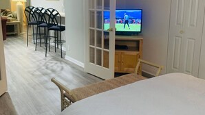 Une chambre d’hôtel comprenant un lit, une télévision, un coin repas avec des chaises et une porte donnant sur une autre pièce.