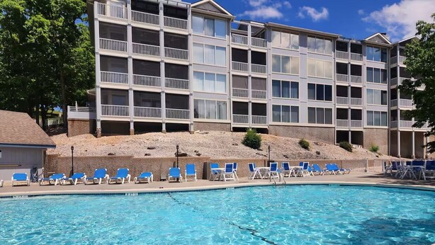 Une piscine avec des chaises longues, un bâtiment doté de balcons et un ciel dégagé.