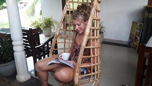 Une personne assise dans un fauteuil en osier, en train de lire un magazine.