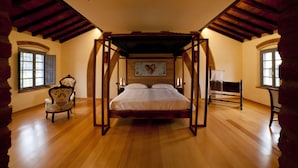 Une chambre à coucher avec un lit à baldaquin, un plancher en bois, une chaise et un tableau accroché au mur.