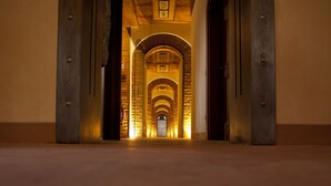 Un couloir aux plafonds voûtés et aux murs de pierre, qui mène à une porte au fond.