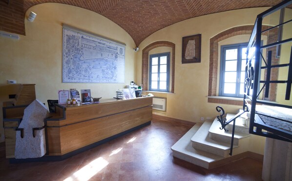 Uma área de recepção com uma mesa de madeira, um mapa grande na parede e uma escada que leva a um andar superior.