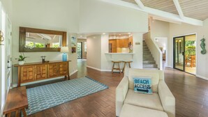 A spacious living room with a wooden bench, a beige armchair, and a blue patterned rug. A wooden cabinet with a mirror and a plant is against the wall. - Open, bright, spacious home with AC in bedrooms, sleeps 9. (Princeville)