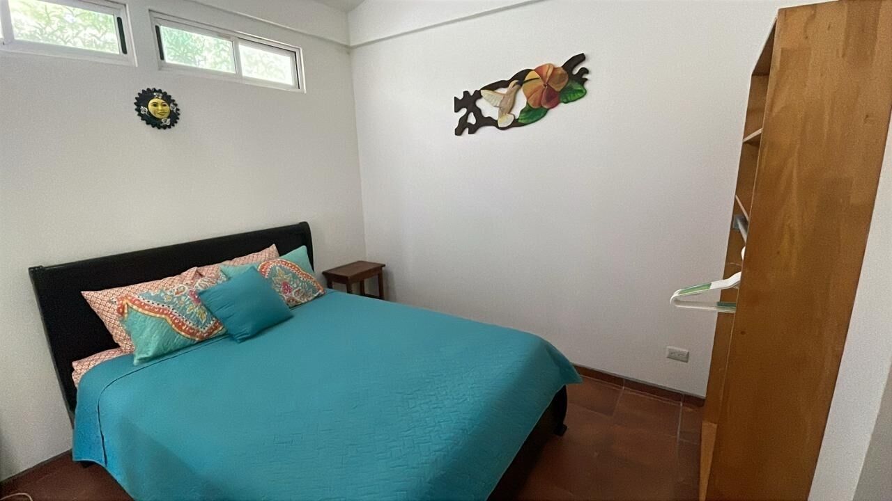 A bedroom with a bed, a small table, a wall decoration, and a door.