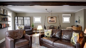 A living room with a brown leather sofa, a white coffee table, and a bookshelf. - 6 Bells: Harbor Springs Lodging for the Discerning Traveler (Harbor Springs)