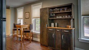 A kitchen with a wooden cabinet, a dining table, chairs, and a window with blinds. - 6 Bells: Harbor Springs Lodging for the Discerning Traveler (Harbor Springs)