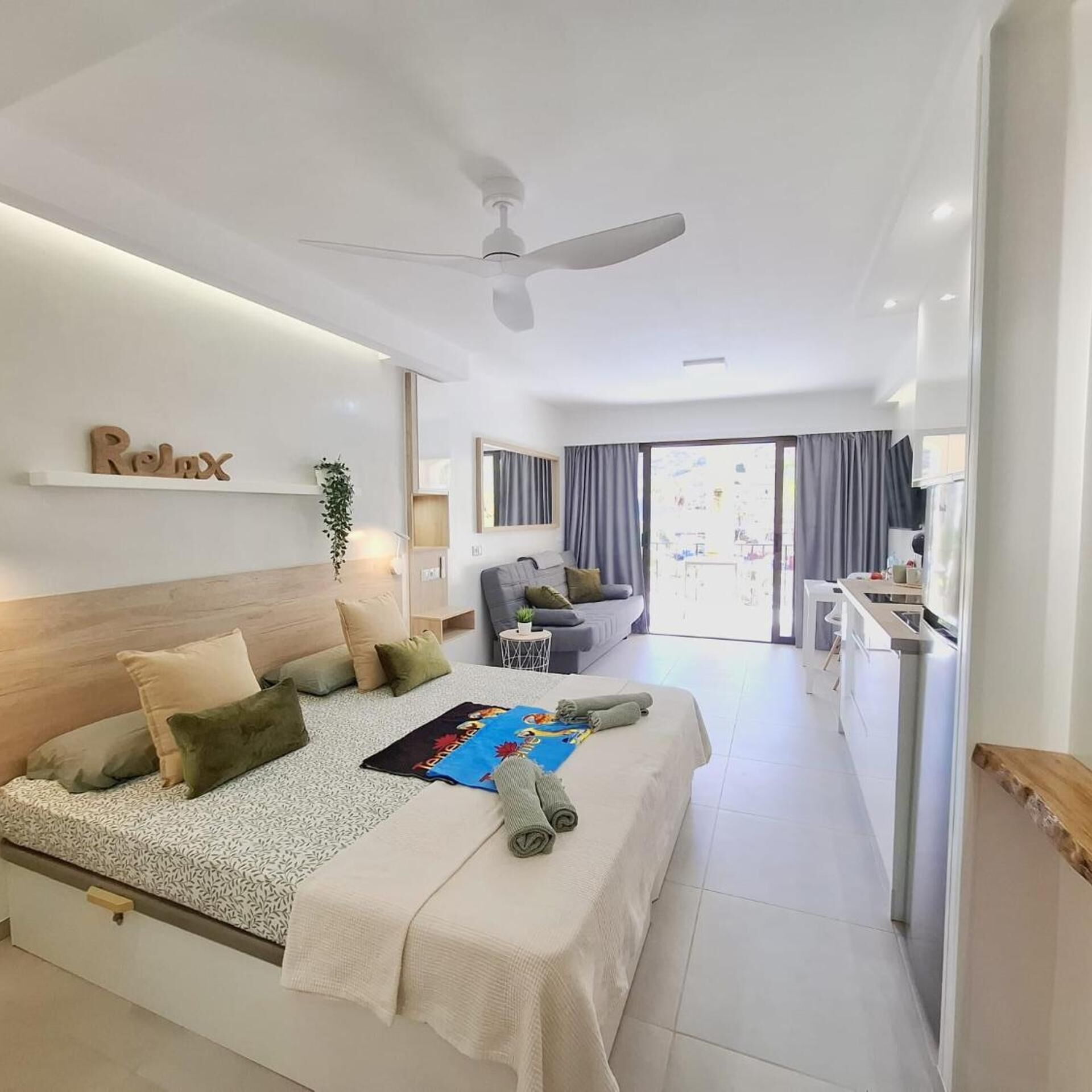 Una habitación de hotel moderna con una cama, un sofá, una mesita y un ventilador de techo.