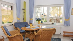 A room with wicker furniture, a round table, and a window with curtains. - Appartementpark Seeblick (Plau am See)