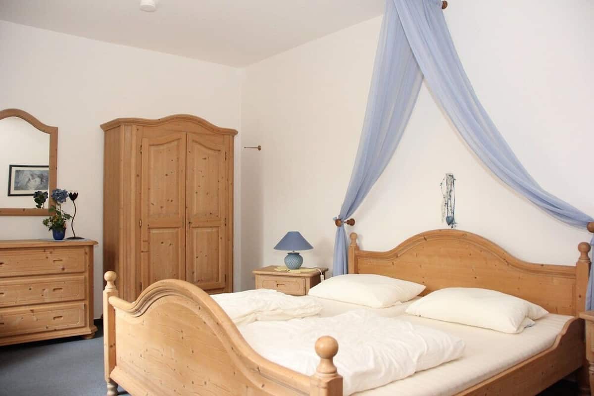 A bedroom with a wooden bed, a nightstand with a lamp, a wardrobe, and a mirror.