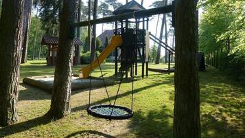 A playground with a swing set and a slide, surrounded by trees.