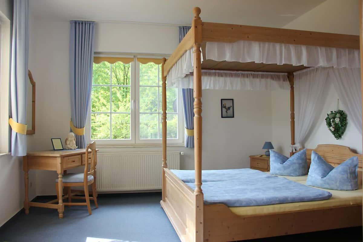 A bedroom with a four-poster bed, a wooden desk, and a chair.
