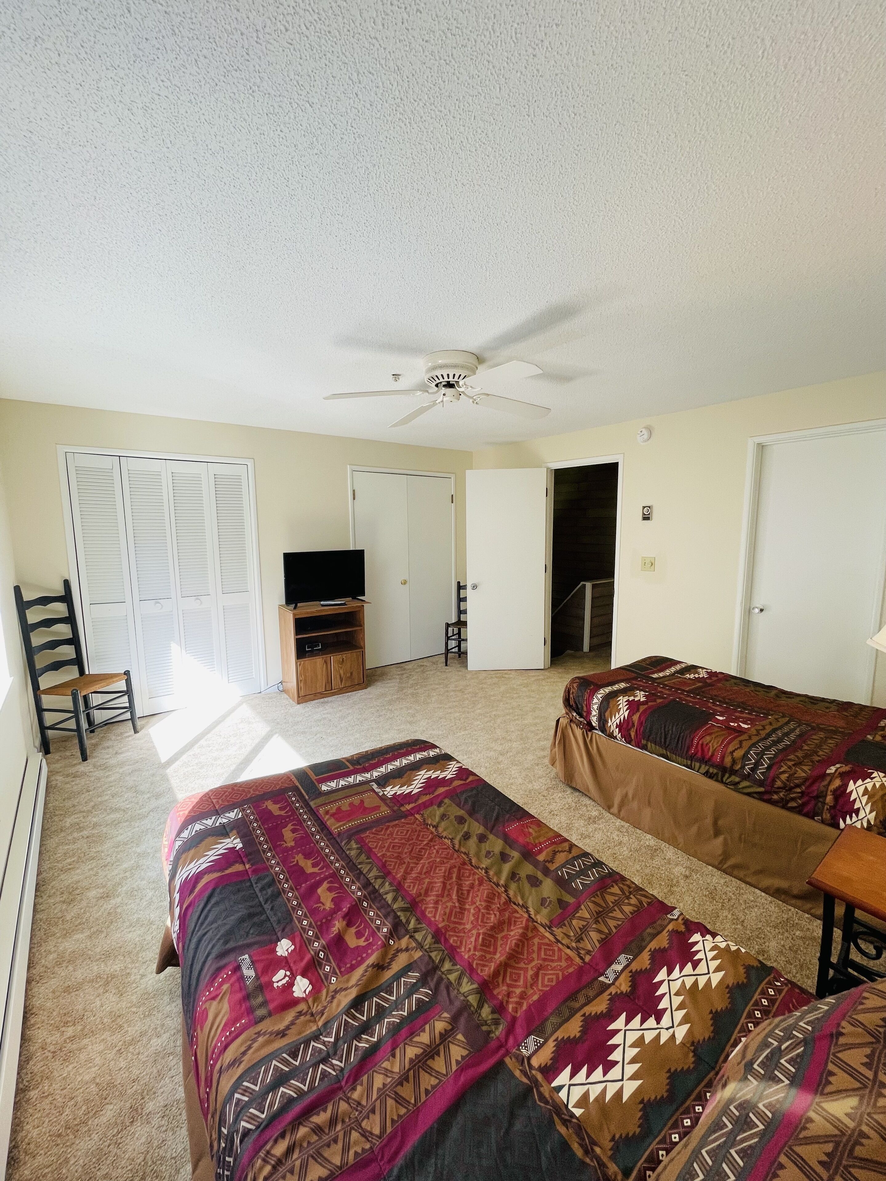 Une chambre avec deux lits, un ventilateur de plafond, une télévision et une armoire.