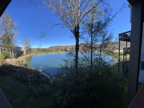 Enjoy serene lakeside views from the multi-level deck with a balcony, surrounded by lush greenery and trees.