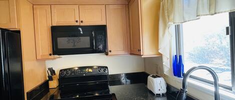 Une cuisine de taille réduite, avec des meubles de rangement en bois, un micro-ondes noir, une cuisinière et un évier.