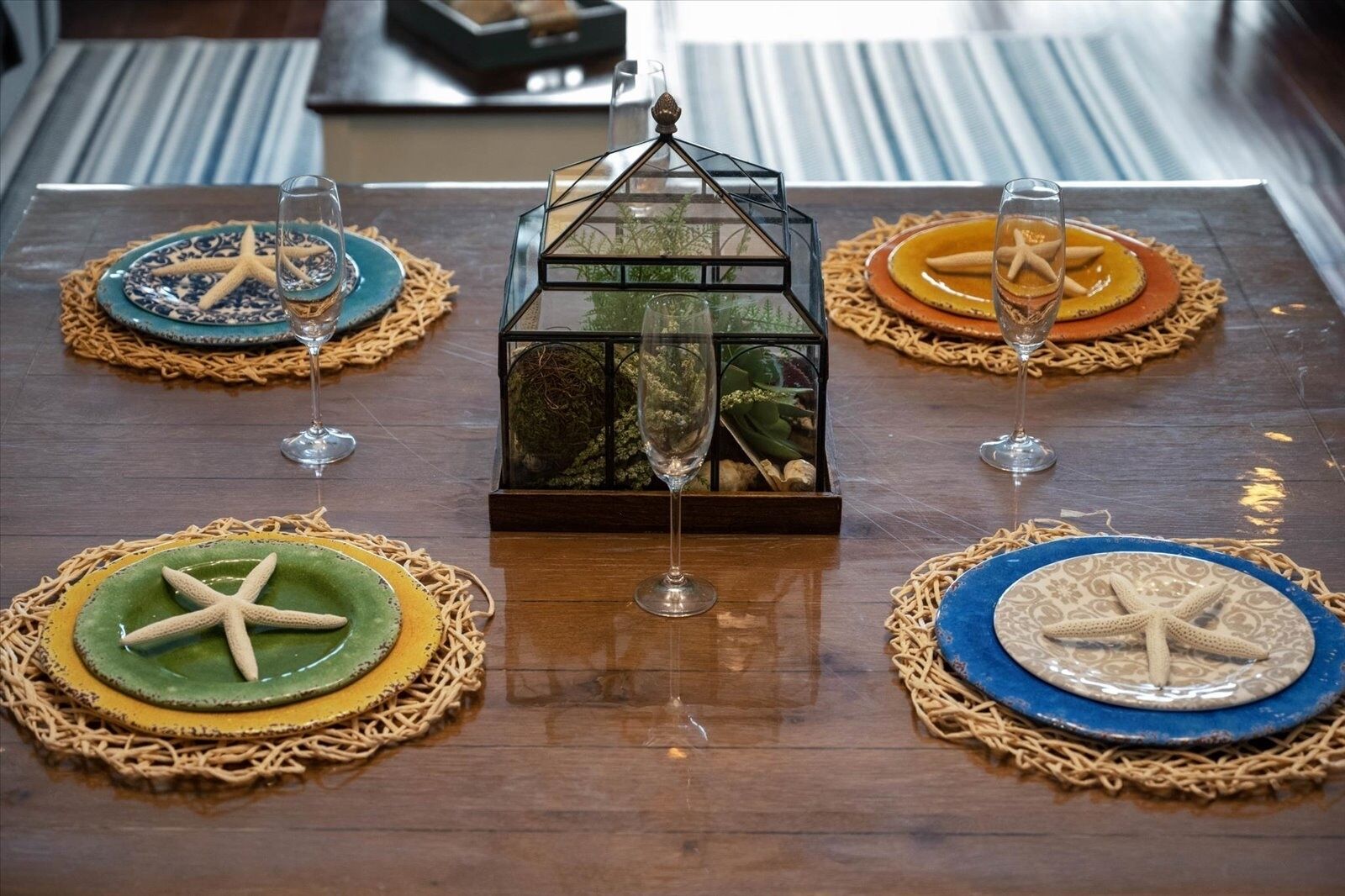A dining table with a central decorative piece surrounded by four plates with starfish designs, each with a glass of water.