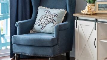 Un fauteuil bleu avec un coussin à motifs, une armoire blanche, une plante et un tableau encadré posés sur une table en bois.