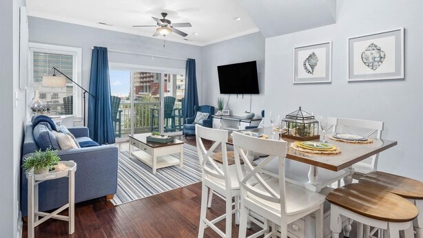 A modern living room with a sofa, coffee table, dining table, and chairs. There is a TV mounted on the wall and artwork displayed above the table. - Beach Paradise III - DOWNTOWN OCEANVIEW Luxury Townhome-Steps to Beach&Boardwalk (Ocean City)