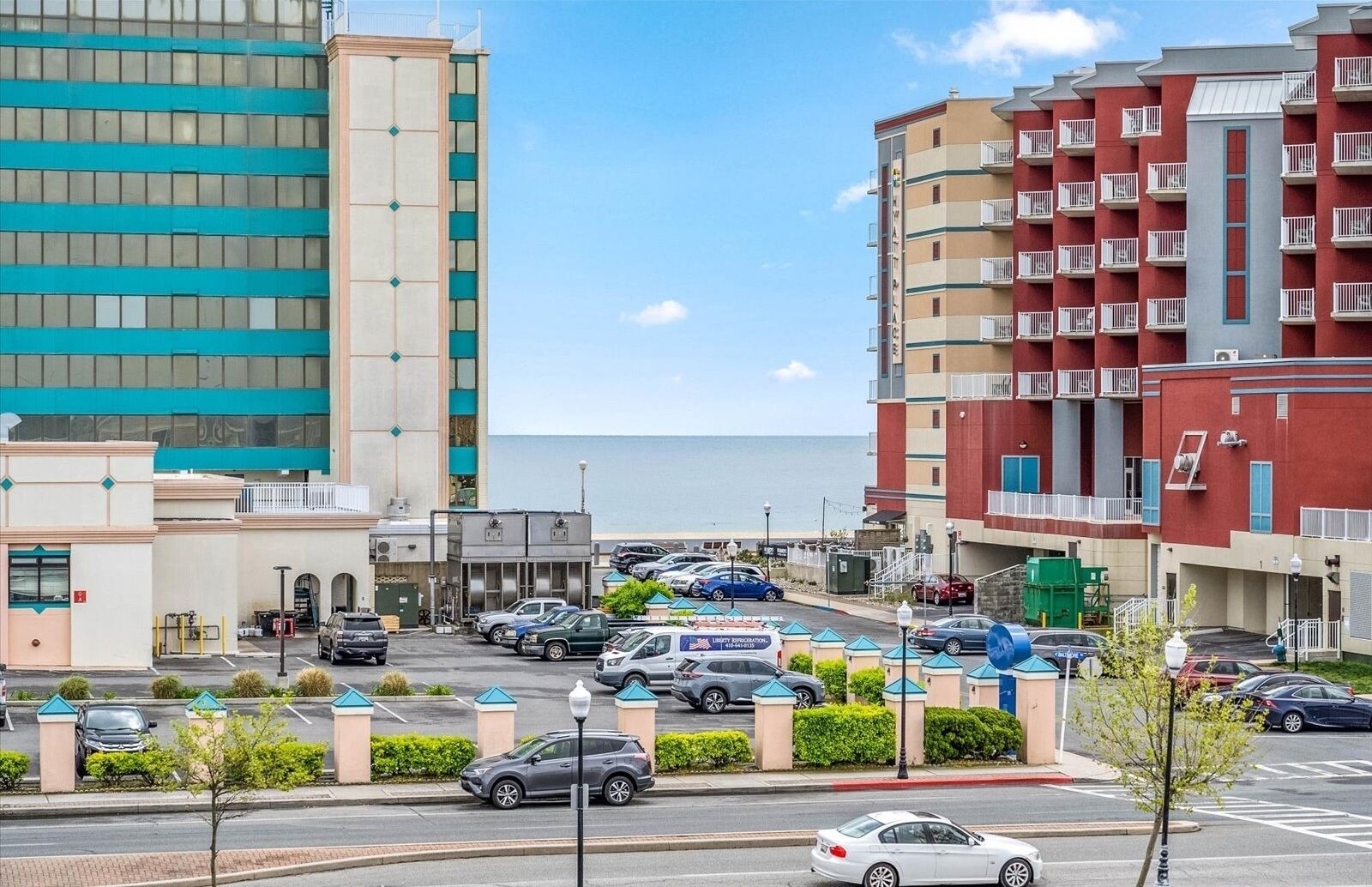 A parking lot with several cars, a building with a sign for 'Liberty Refrigeration', and a view of the ocean.