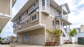A multi-story residential building with a garage entrance, a balcony on the second floor, and a small tree in front. - Beach Paradise III - DOWNTOWN OCEANVIEW Luxury Townhome-Steps to Beach&Boardwalk (Ocean City)