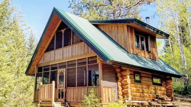 Une cabane en rondins avec un toit à forte pente, de grandes fenêtres et une véranda.