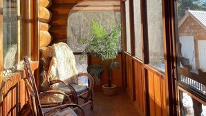 L’intérieur d’une cabane en rondins, avec des murs en bois, de grandes fenêtres et un coin salon comprenant des chaises et une table.