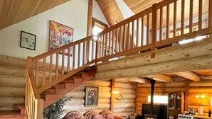 L’intérieur d’une cabane en rondins, avec un escalier en bois, une cheminée, un canapé et un coin repas.
