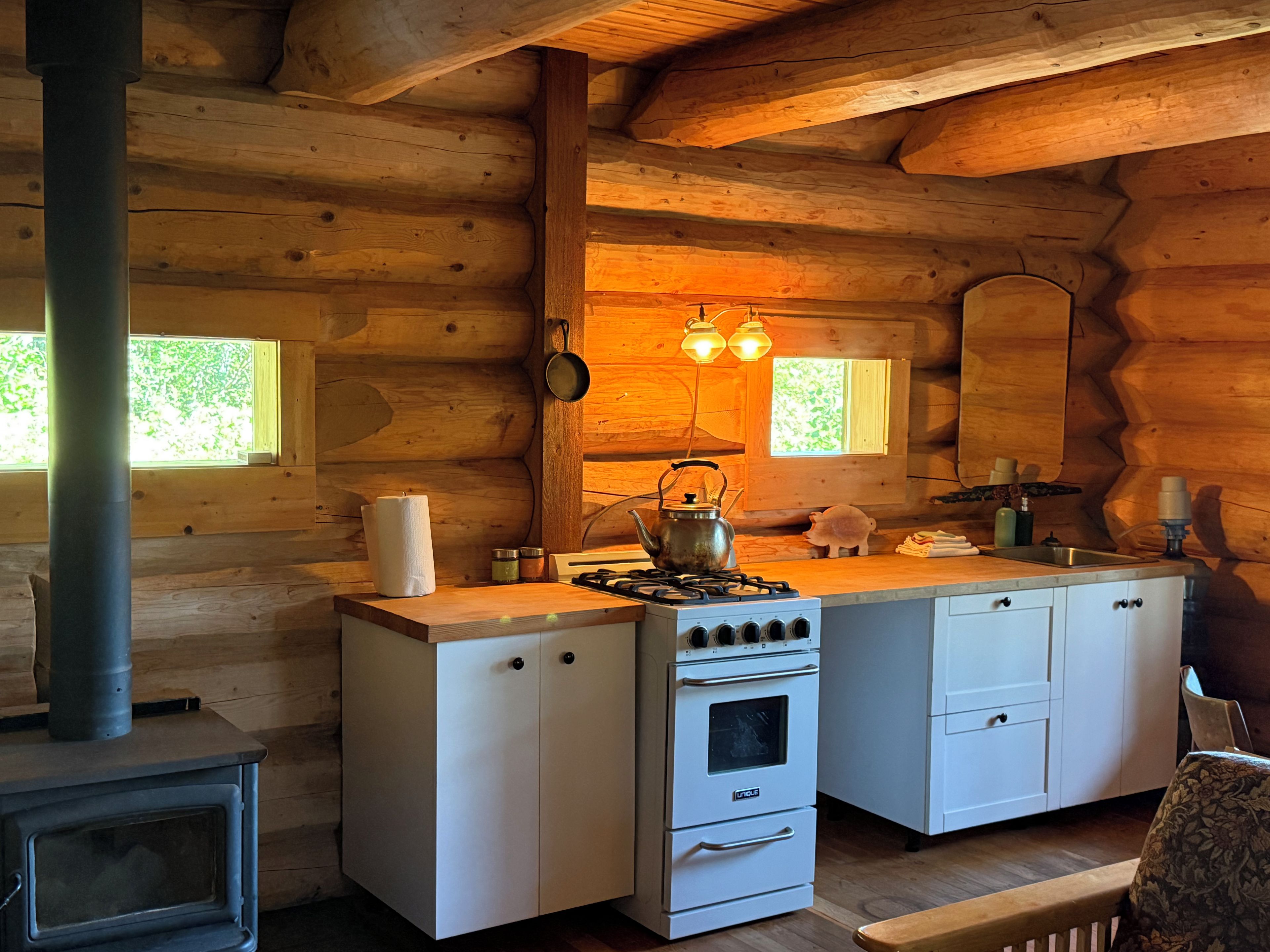 Eine Kücheneinrichtung in einer Blockhütte mit Holzofen, Herd, Spüle und Schränken.