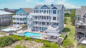 A large, multi-story building with a pool, multiple balconies, and a view of the ocean. - Luxury Oceanfront Home w/ Pool, HotTub, EV Charger, Elevator, Theater, Much More (Hatteras)