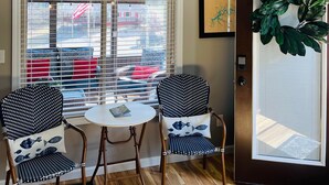 A room with two chairs and a small table, a large window with blinds, a door with a plant, and a wall-mounted sign that reads "gather". - Lake Cumberland Hideaway #1-2 miles from Jtown Marina! Boat Parking & Fire Pit! (Jamestown)