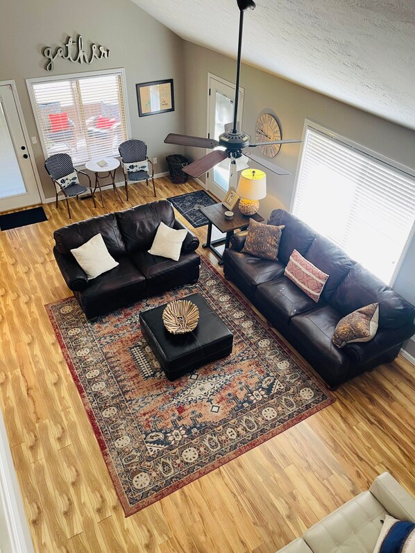 A living room with two black leather sofas, a patterned rug, a ceiling fan, and a window with blinds. - Lake Cumberland Hideaway #1-2 miles from Jtown Marina! Boat Parking & Fire Pit! (Jamestown)