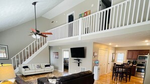 A spacious living area with a high ceiling, a black leather sofa, a wooden coffee table, and a dining area with a kitchen in the background. - Lake Cumberland Hideaway #1-2 miles from Jtown Marina! Boat Parking & Fire Pit! (Jamestown)