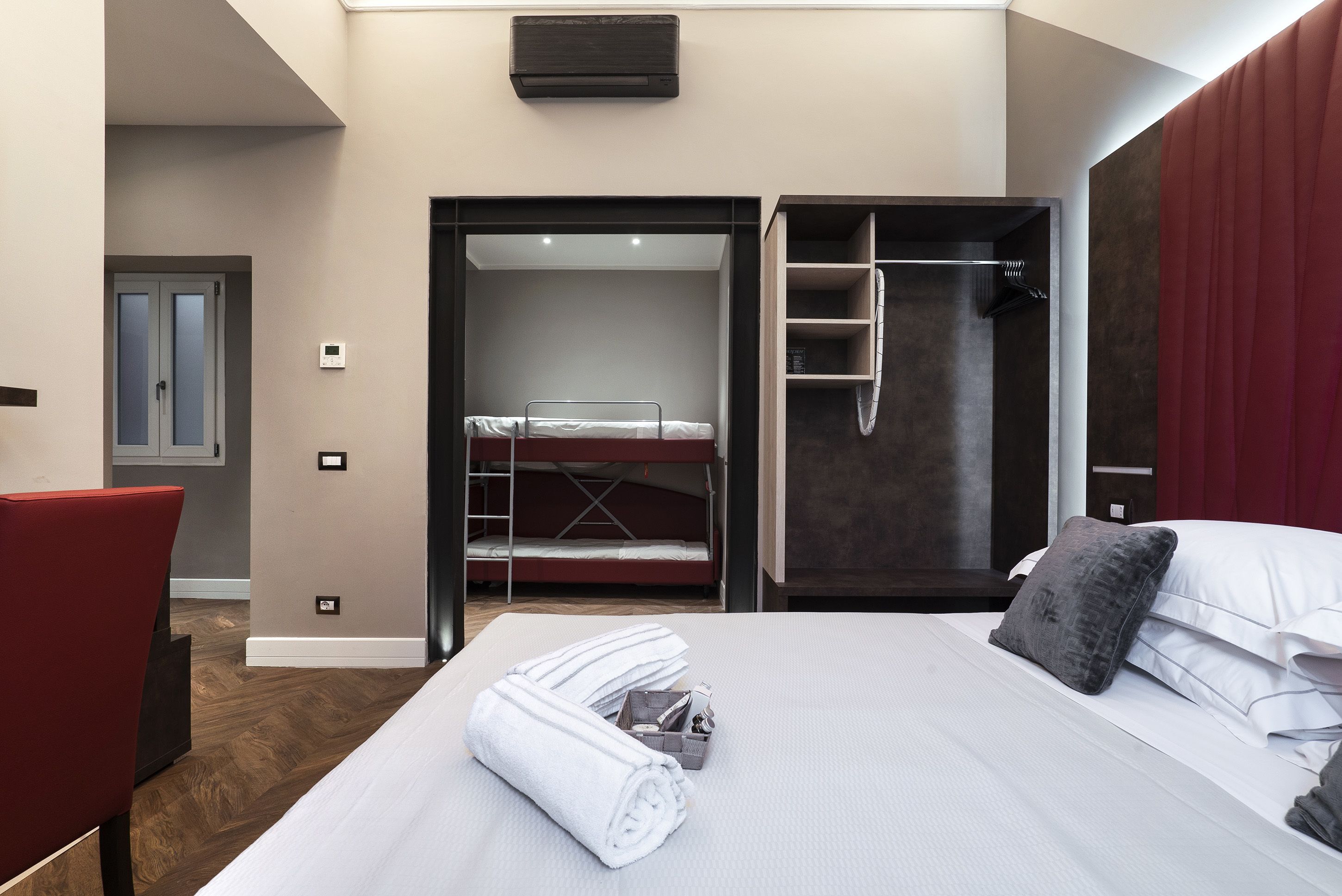 Ein modernes Hotelzimmer mit einem Etagenbett, einer Dusche, einem roten Sessel und ordentlich gefalteten Handtüchern auf dem Bett.