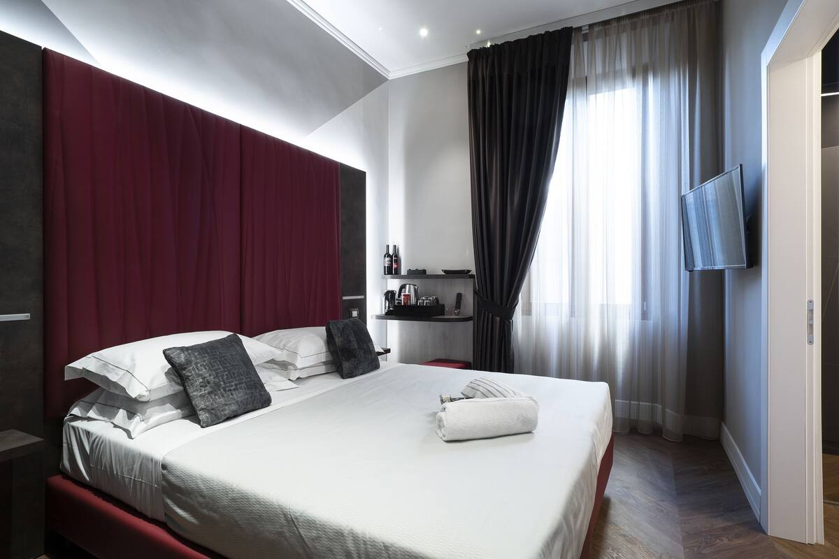 A modern hotel room with a large bed, a TV mounted on the wall, and a small desk with a chair.