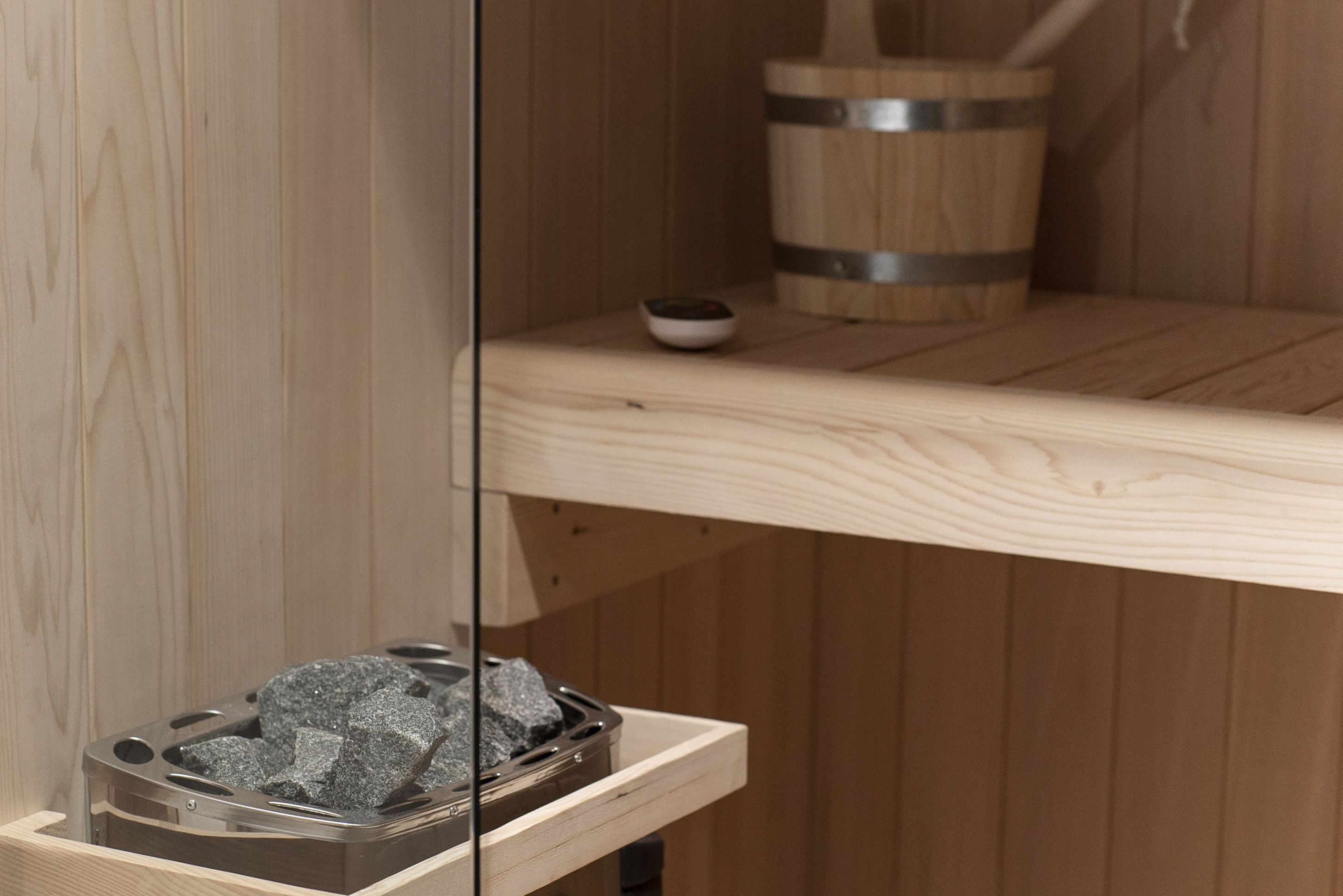 A wooden sauna with a metal basin filled with stones, a small bowl, and a wooden bucket.
