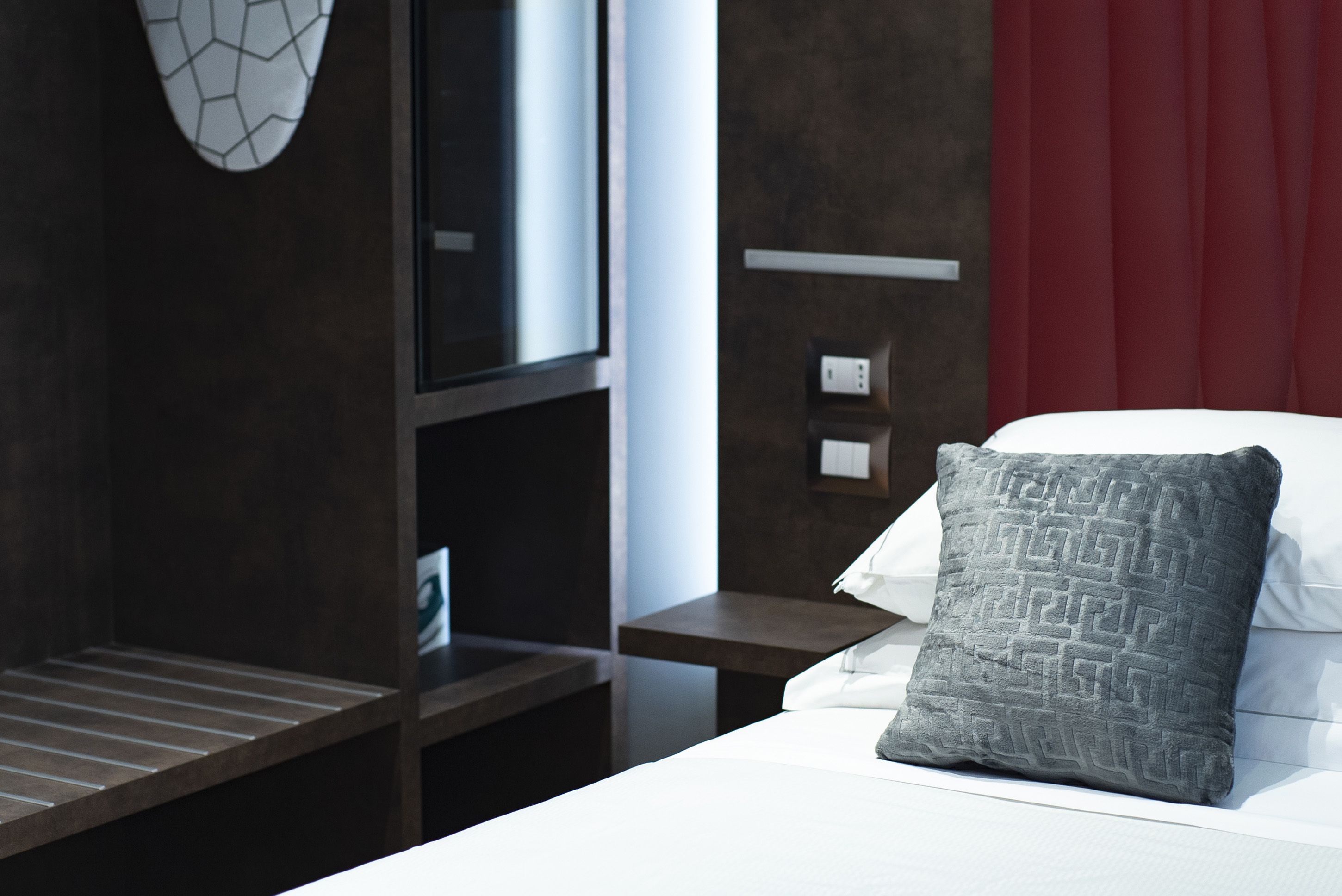 A hotel room with a bed, a TV, a red curtain, and a nightstand with a lamp.